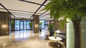 A spacious lobby with a marble floor, large windows, and indoor plants.