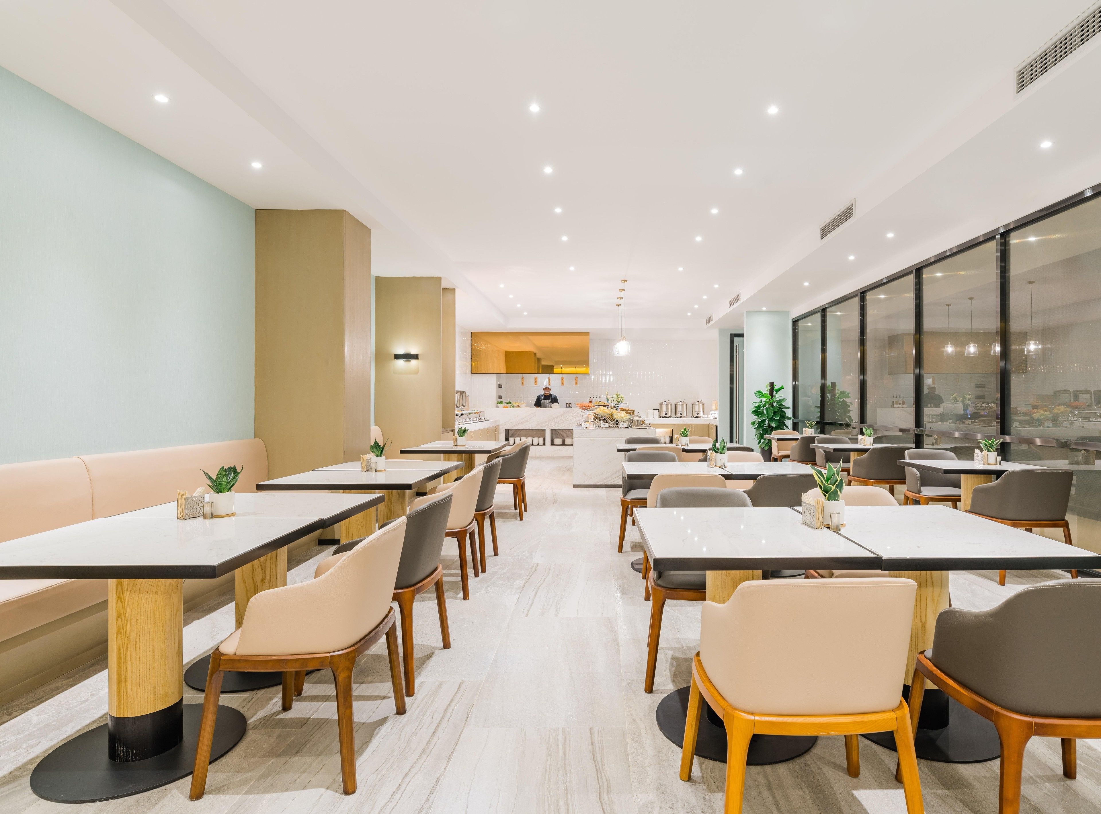 A modern dining area with multiple tables and chairs, a central island with a bar, and large windows providing natural light.
