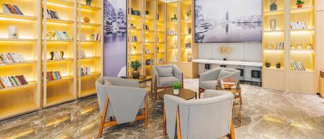 A spacious reading area with multiple wooden bookshelves, comfortable seating, and a large wall-mounted TV.