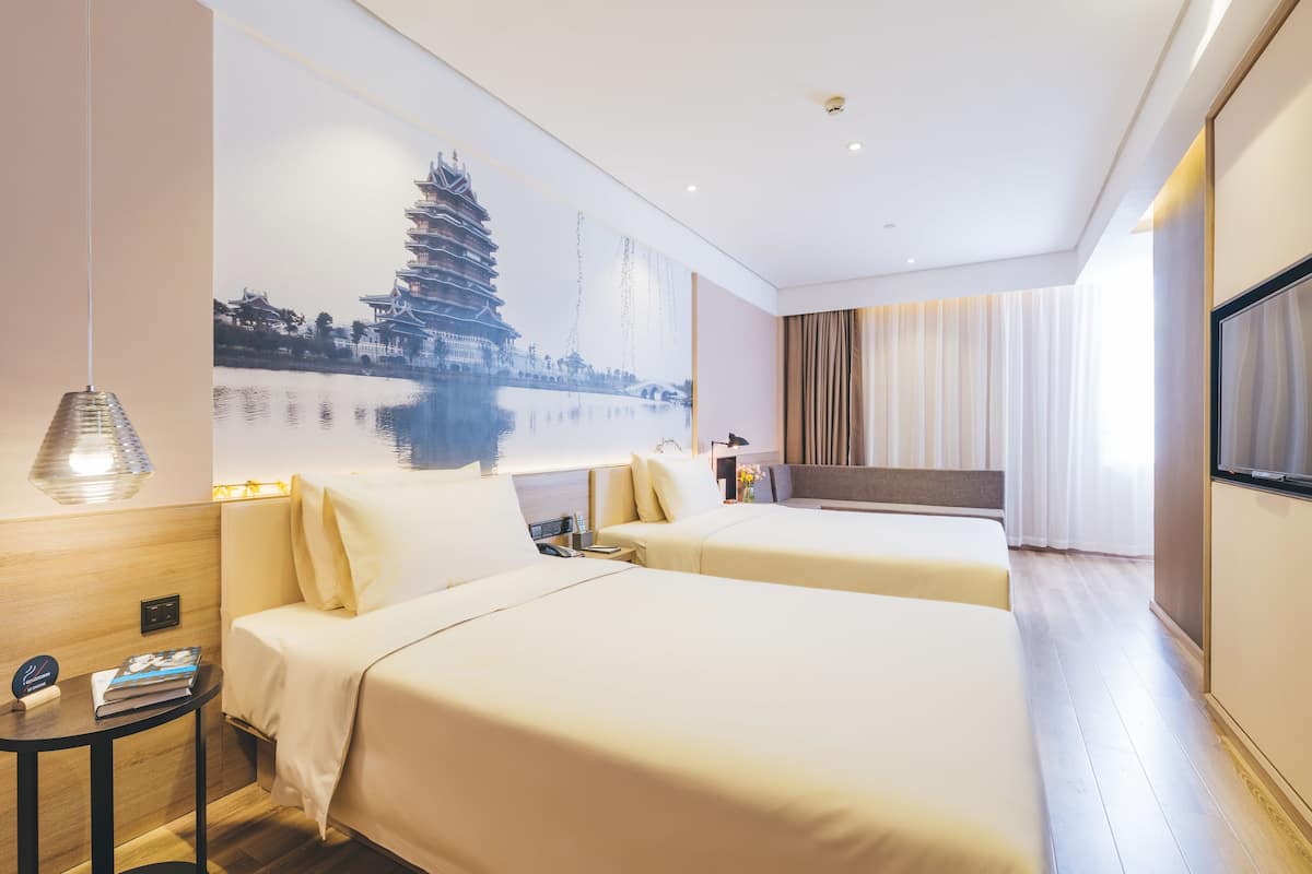 Quarto de hotel com duas camas, um mural grande na parede, uma televisão e uma mesinha de cabeceira.