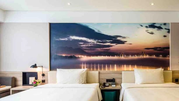 A hotel room with two beds, a large painting of a sunset over water, and a wooden headboard. - Atour Hotel People's Square Xiaoshan Hangzhou (Hangzhou)