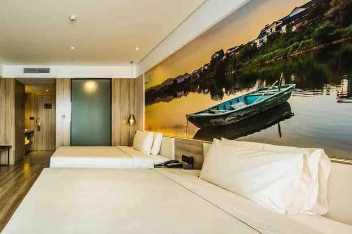 Ein modernes Hotelzimmer mit einem großen Bett, einem Flachbildfernseher, einem Gemälde eines Sees und Holzboden.