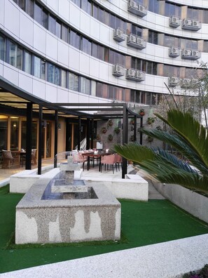 A modern building with a curved facade, outdoor seating area with tables and chairs, a water feature, and potted plants. - Atour Hotel Tianyi Square Ningbo (Ningbo)