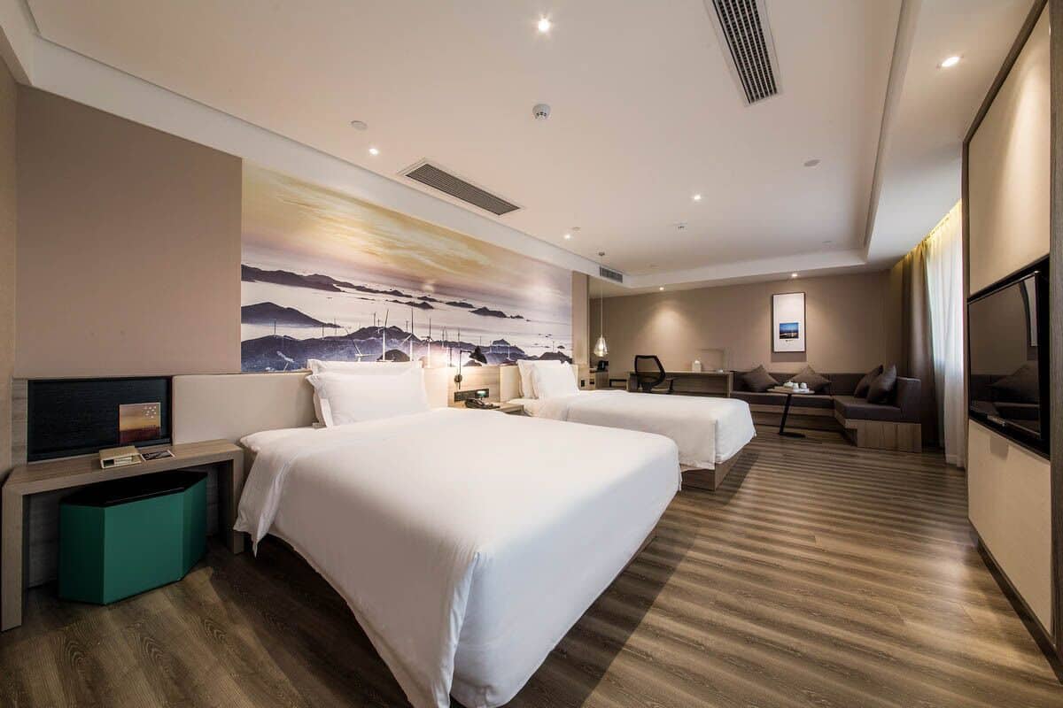 Habitación de hotel con dos camas, un escritorio, una silla, un televisor y un cuadro en la pared.