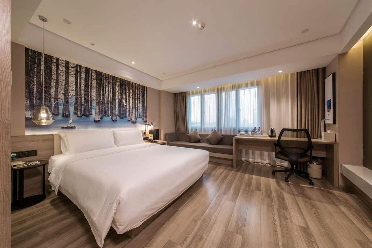 Una habitación de hotel moderna con una cama grande, un sofá, un escritorio y un ventanal con cortinas.