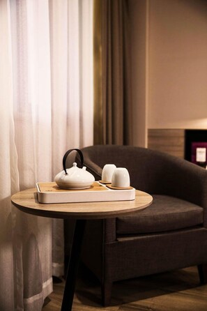 A modern hotel room with a round wooden table featuring a white teapot and cups, a dark armchair, and sheer curtains. - Atour Hotel Tianyi Square Ningbo (Ningbo)