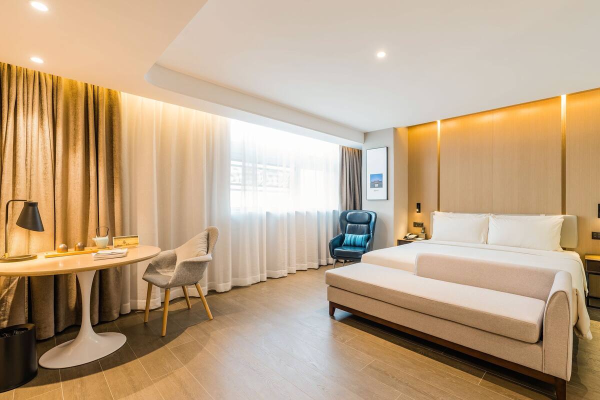 Une chambre d’hôtel avec un lit, un bureau, une chaise et une grande fenêtre avec des rideaux.