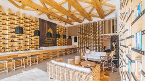 Un interior moderno con vigas de madera, estanterías llenas de libros y botellas, muebles de mimbre y una encimera de mármol.
