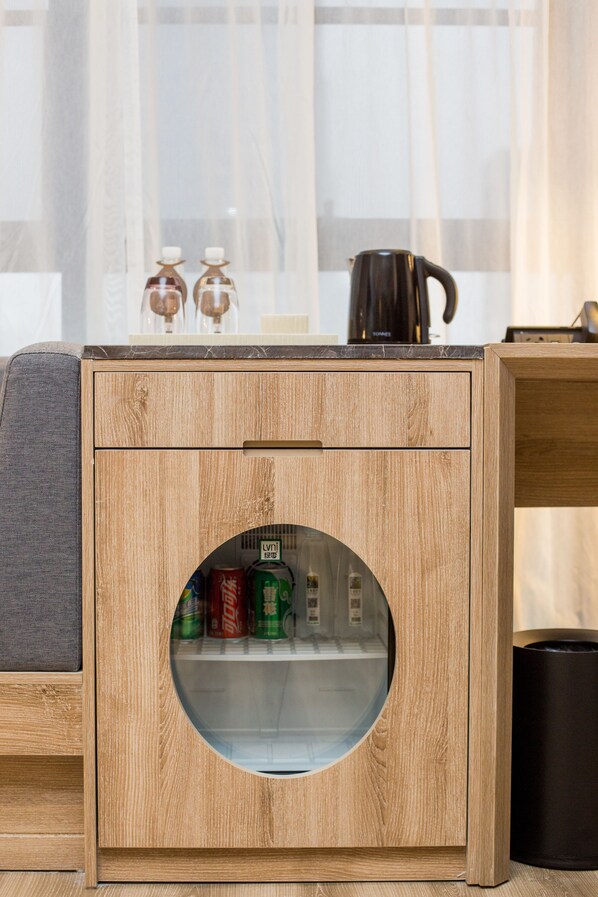 Un mueble de madera con puerta redonda de vidrio, que contiene latas y una botella.