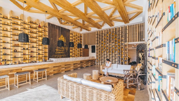 A modern interior with wooden beams, shelves of books and bottles, wicker furniture, and a marble counter. - Atour S Hotel Huandao Road Xiamen (Xiamen)
