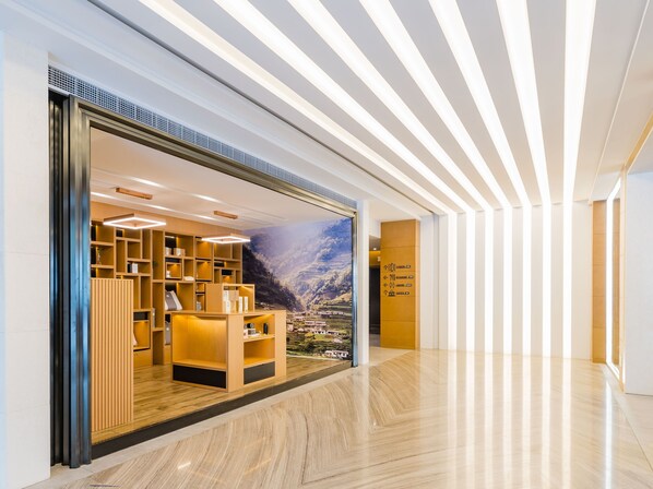 A hotel lobby with a large display window showcasing a mountainous landscape. Inside, there is a reception desk with a wooden finish and a seating area with cushioned chairs. - Atour S Hotel Huandao Road Xiamen (Xiamen)