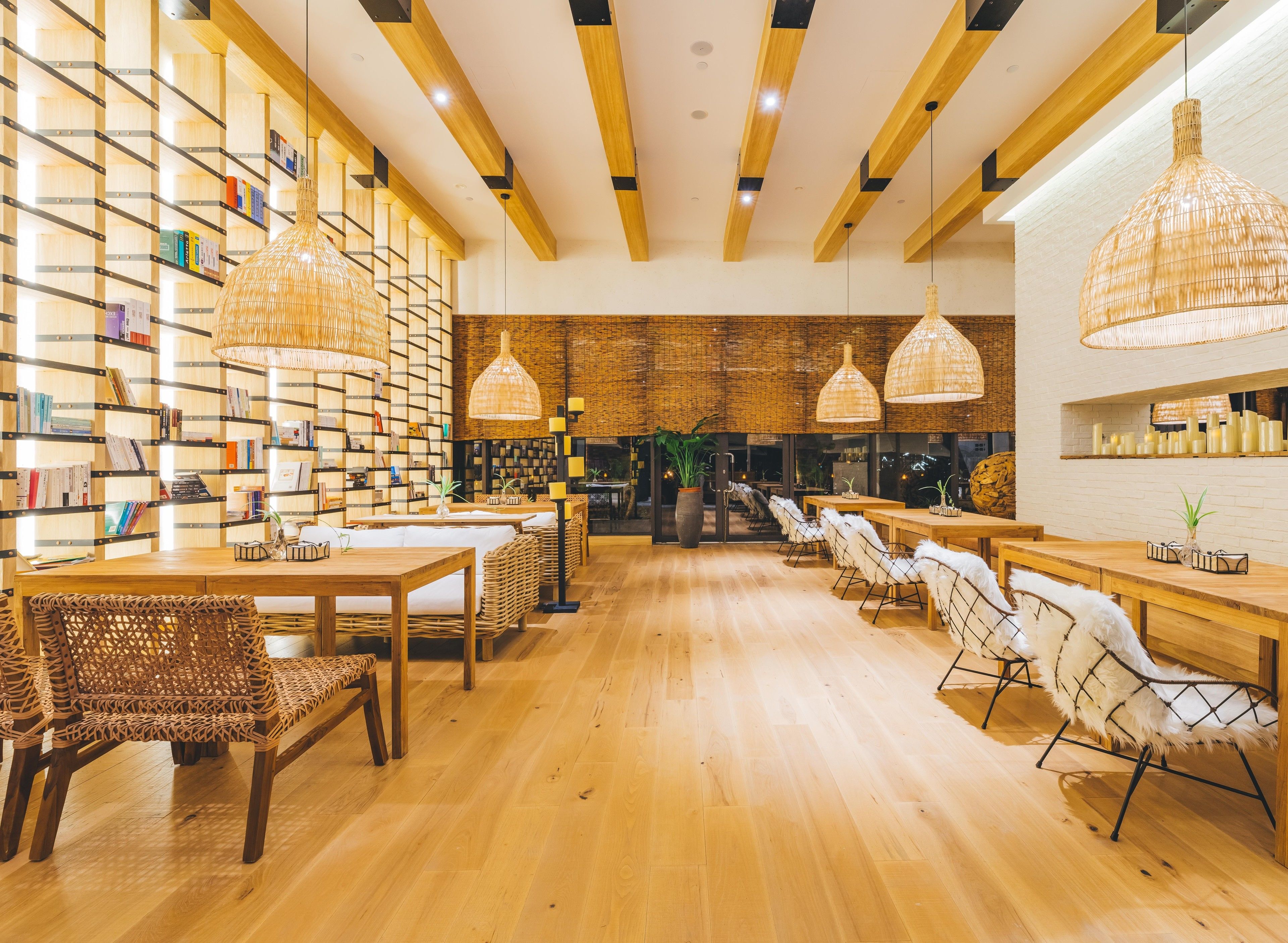 A modern library with wooden bookshelves, wicker furniture, and hanging lamps.