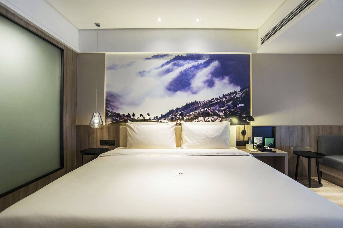 A modern hotel room with a large bed, a nightstand, a desk, and a chair.