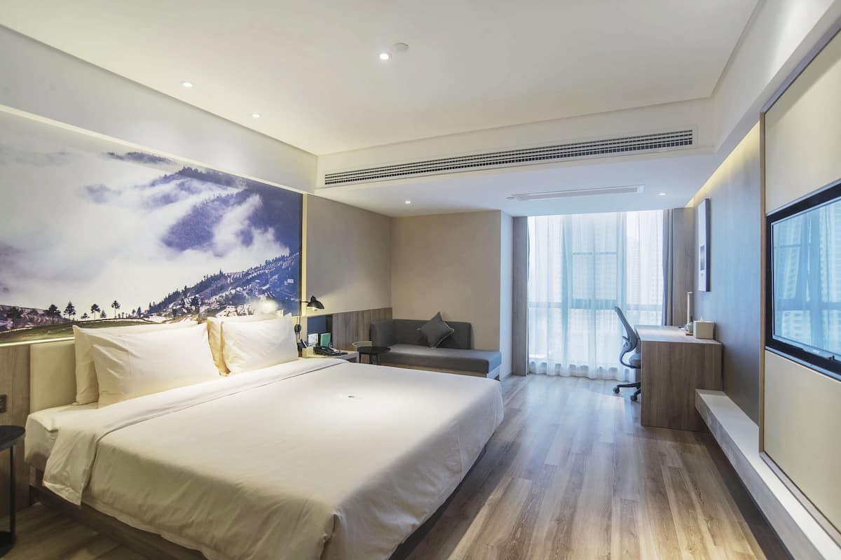 A modern hotel room with a large bed, a desk, and a view of the city.