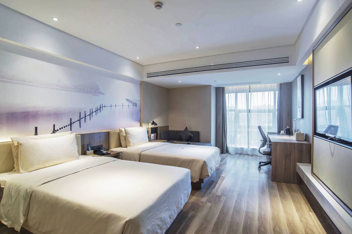 A hotel room with two beds, a desk, a chair, and a large window.
