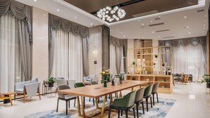 Un espace repas moderne avec une longue table en bois, plusieurs chaises et une bibliothèque en arrière-plan.