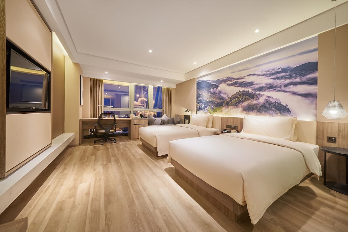 A hotel room with two beds, a desk, a chair, and a large scenic wall mural.