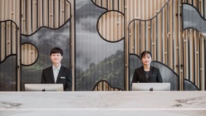 Deux personnes sont assises derrière un comptoir d’accueil au design moderne, doté d’un panneau arrière en bois et d’un plateau en marbre.