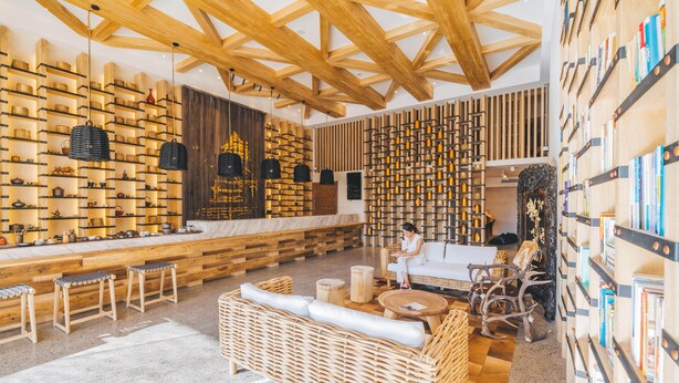 Een modern interieur met houten balken, boekenkasten en flessen, rieten meubels en een marmeren aanrecht.