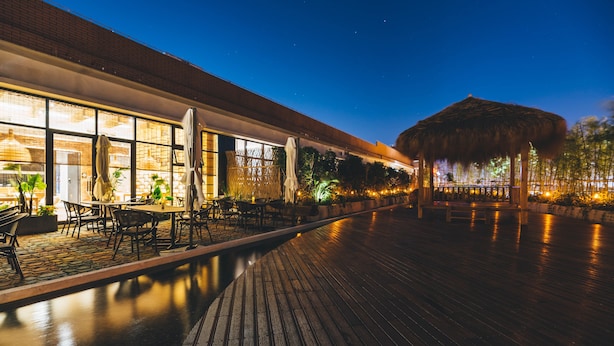 An outdoor dining area with tables and chairs, a pool, and a thatched-roof structure. - Atour Hotel Taiguhui of Tianhe River Guangzhou (Guangzhou)