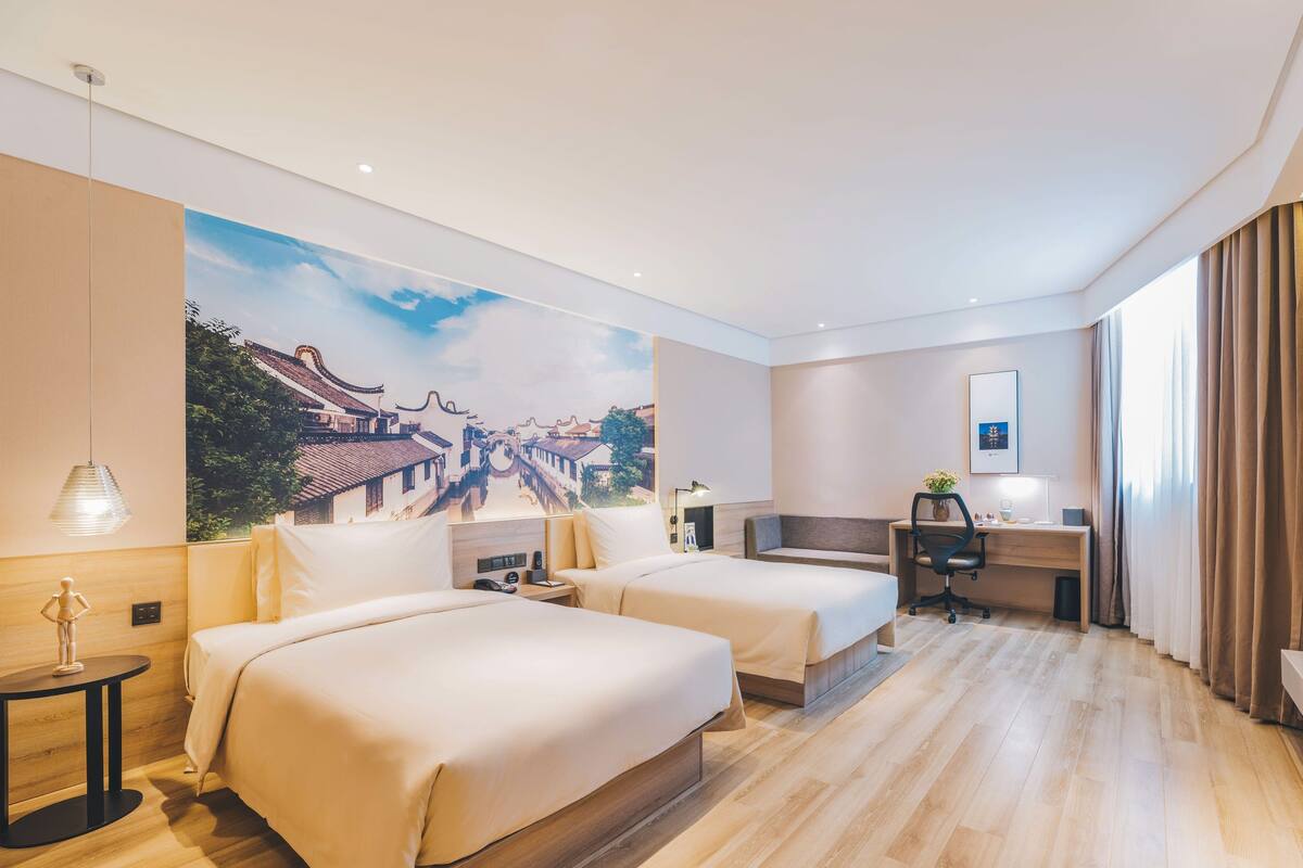 Habitación de hotel con dos camas, un escritorio, una silla, una lámpara y un mural grande en la pared.