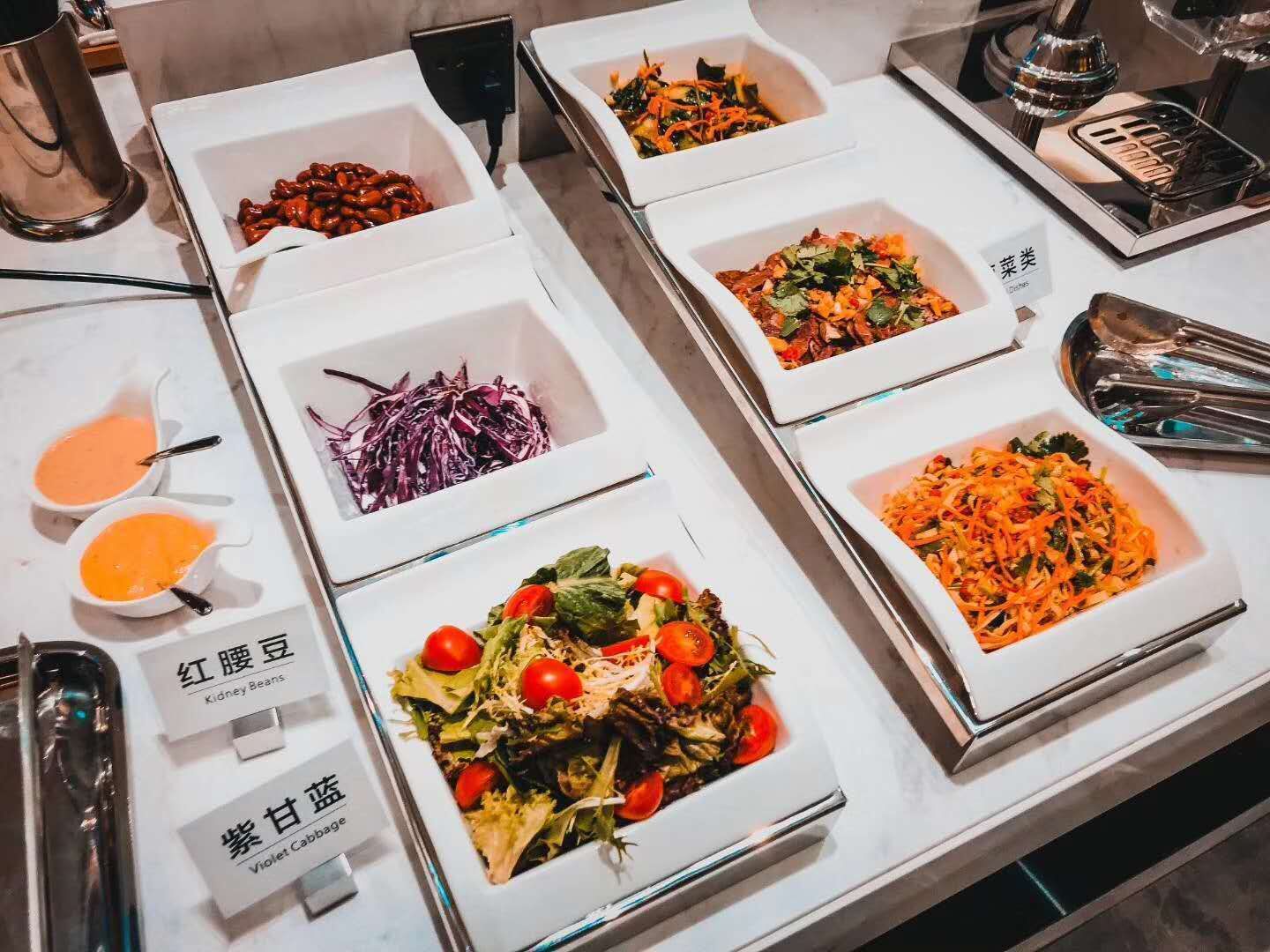 A buffet table with various dishes, including kidney beans, a salad with cherry tomatoes, and a dish with shredded carrots.