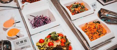 A buffet table with various dishes, including kidney beans, a salad with cherry tomatoes, and a dish with shredded carrots.