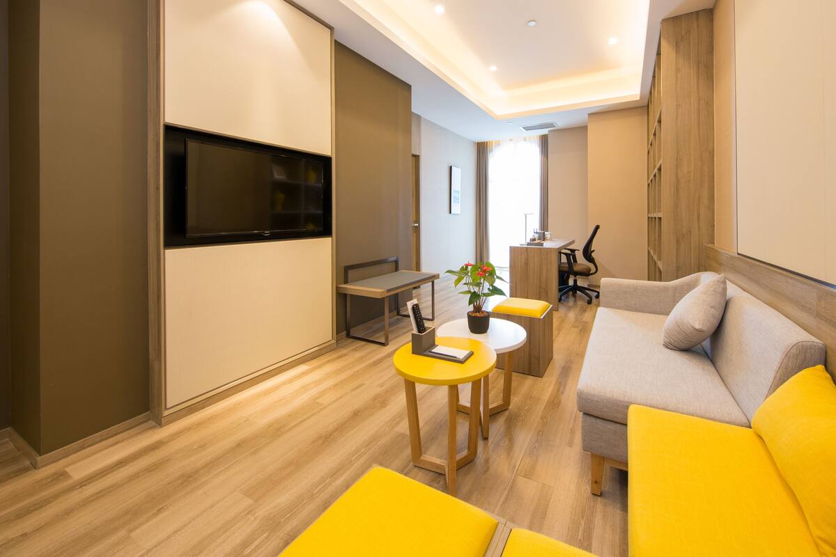 A modern living room with a sofa, yellow cushions, a small table, a TV, and a potted plant.