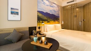 Une chambre d’hôtel comprenant un lit, un canapé, une petite table avec un vase et des salières, une lampe et une fresque murale représentant un paysage de montagne.