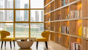 Un intérieur moderne avec une grande fenêtre, deux fauteuils jaunes, une table basse blanche et une bibliothèque en bois remplie de livres.