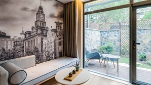 A modern living room with a large cityscape mural, a sofa, a small table with a tray, and a sliding glass door leading to an outdoor patio. - Atour Hotel Hongen Road Forest Park Chongqing (Chongqing)