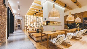 A modern interior with a long hallway leading to a seating area with tables and chairs, wooden beams on the ceiling, and a brick wall on one side. - Atour Hotel Nanbin Road Chongqing (Chongqing)