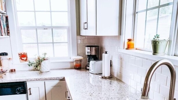 A kitchen with white cabinets, a stainless steel sink, a coffee maker, and a window with a view of the outdoors.
