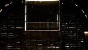 A person standing in a wooden barn with a large open door at the end.