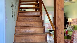 A wooden staircase with a wooden handrail, leading to a room with a ceiling fan and a green couch.