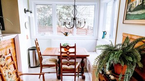 A cozy dining area with a wooden table and chairs, a chandelier, and a view of a snowy garden through large windows.