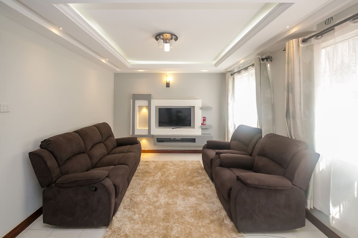 A modern living room with two brown sofas, a beige rug, a flat-screen TV, and a ceiling light fixture.