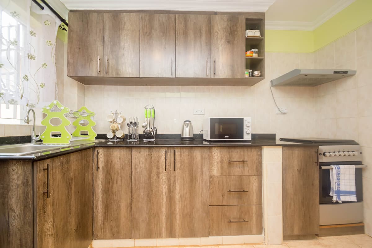 A kitchen with wooden cabinets, a microwave, a kettle, and a stove.