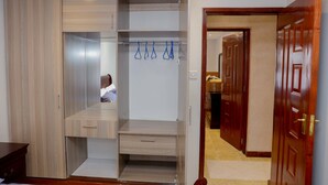 A walk-in closet with wooden doors, a hanging rack, and a bench. - Esterina Suites (Nairobi)