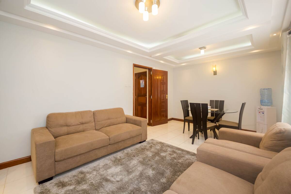 A living room with a beige sofa, a coffee table, and a dining area with a table and chairs.