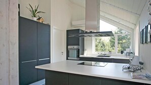 A modern kitchen with dark cabinetry, a built-in oven, and a large window providing a view of the outdoors. - Amazing home in Højby with sauna (Højby)