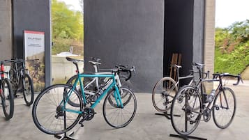 Bicycles parked in an outdoor area with a concrete floor and a black wall in the background.