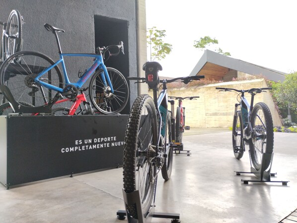 Bicicletas estacionadas en un espacio interior con piso de concreto y pared negra con texto.