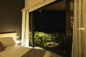 A bedroom with a large bed, a nightstand with a lamp, and a view of an outdoor garden area with a table and chairs. - Hotel Casa Du Velo (Filandia)