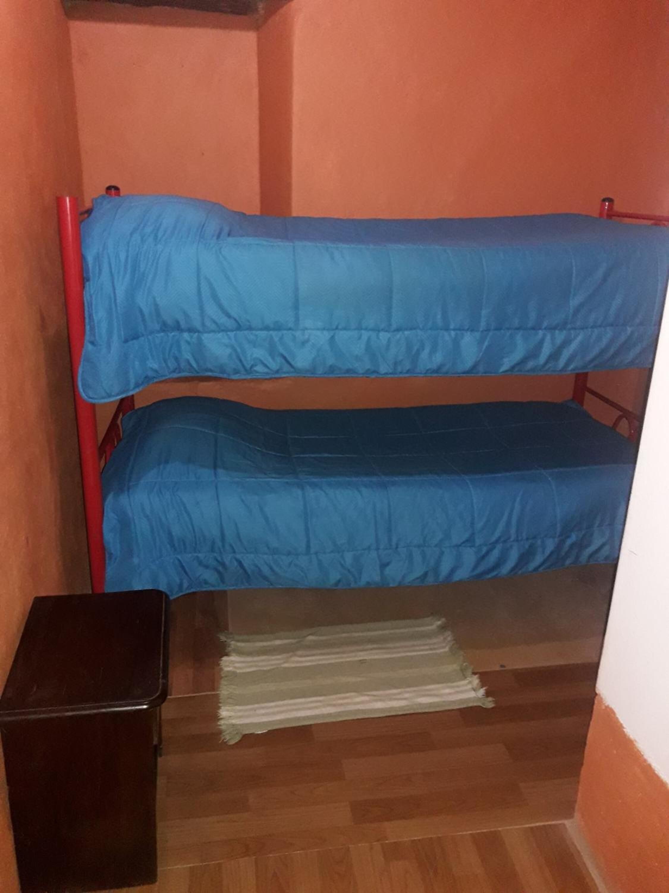 A bunk bed with blue bedding in a room with wooden flooring and orange walls.