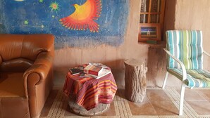 Una habitación acogedora con un sofá de cuero marrón, un sillón a rayas, una mesa redonda con mantel de colores y un mural de un pájaro volando bajo un cielo estrellado.