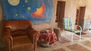 Una habitación con un sofá de cuero marrón, una silla a rayas, una mesita redonda con mantel de tela estampado en rojo y blanco, y un mural con un cielo nocturno lleno de estrellas y una luna creciente.