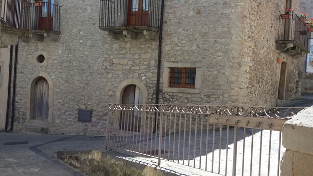 Un edificio de piedra con varios balcones, una entrada con reja y un pequeño patio.