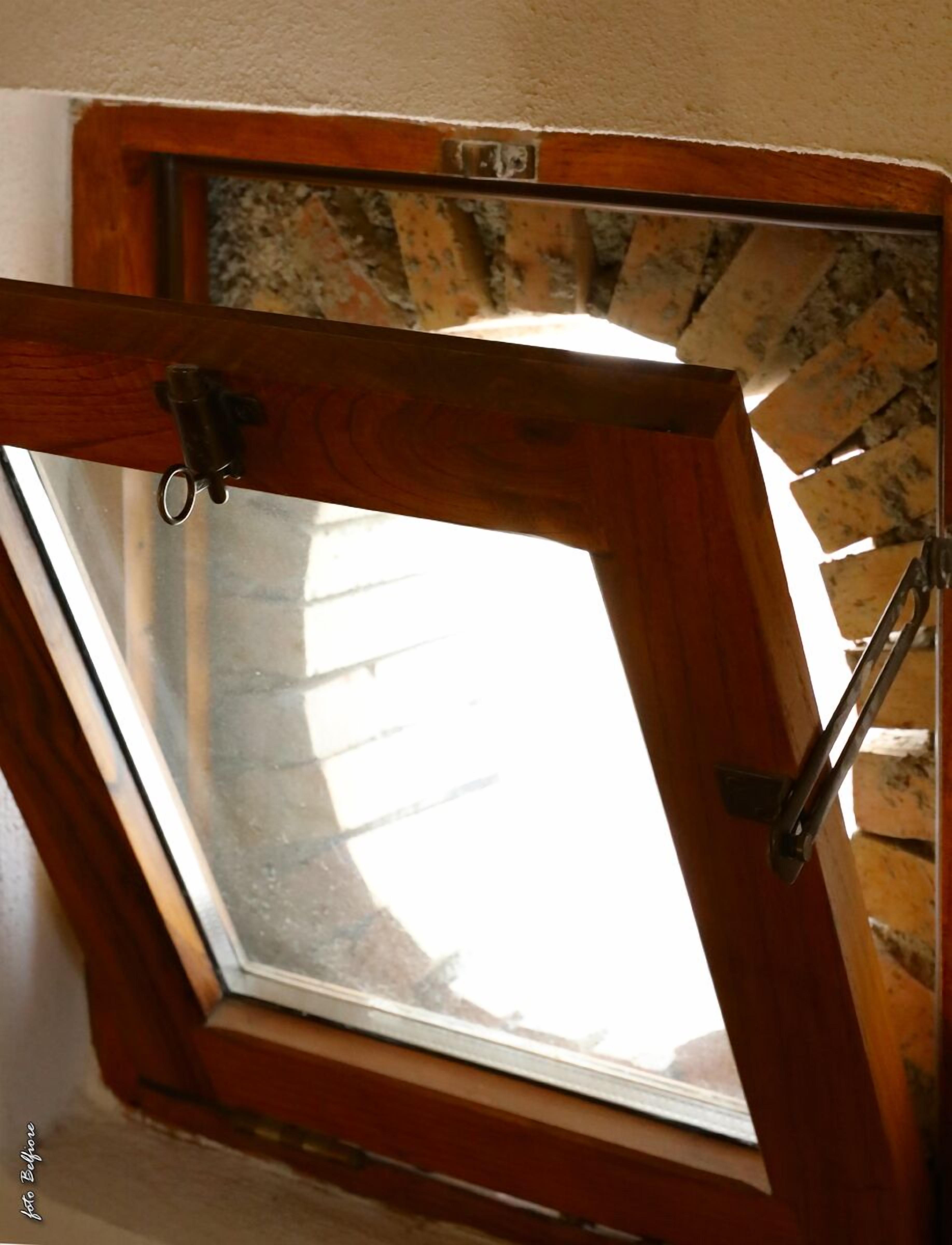 Une lucarne dotée d’un cadre en bois et de charnières en métal, fixée à un mur en briques.