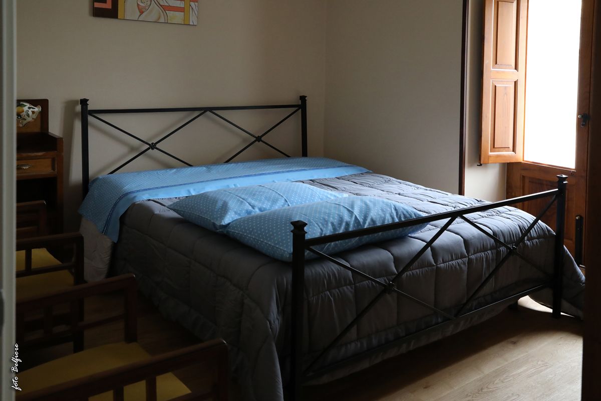 A single bed with a metal frame and a blue quilt, a wooden nightstand, and a wooden chair.